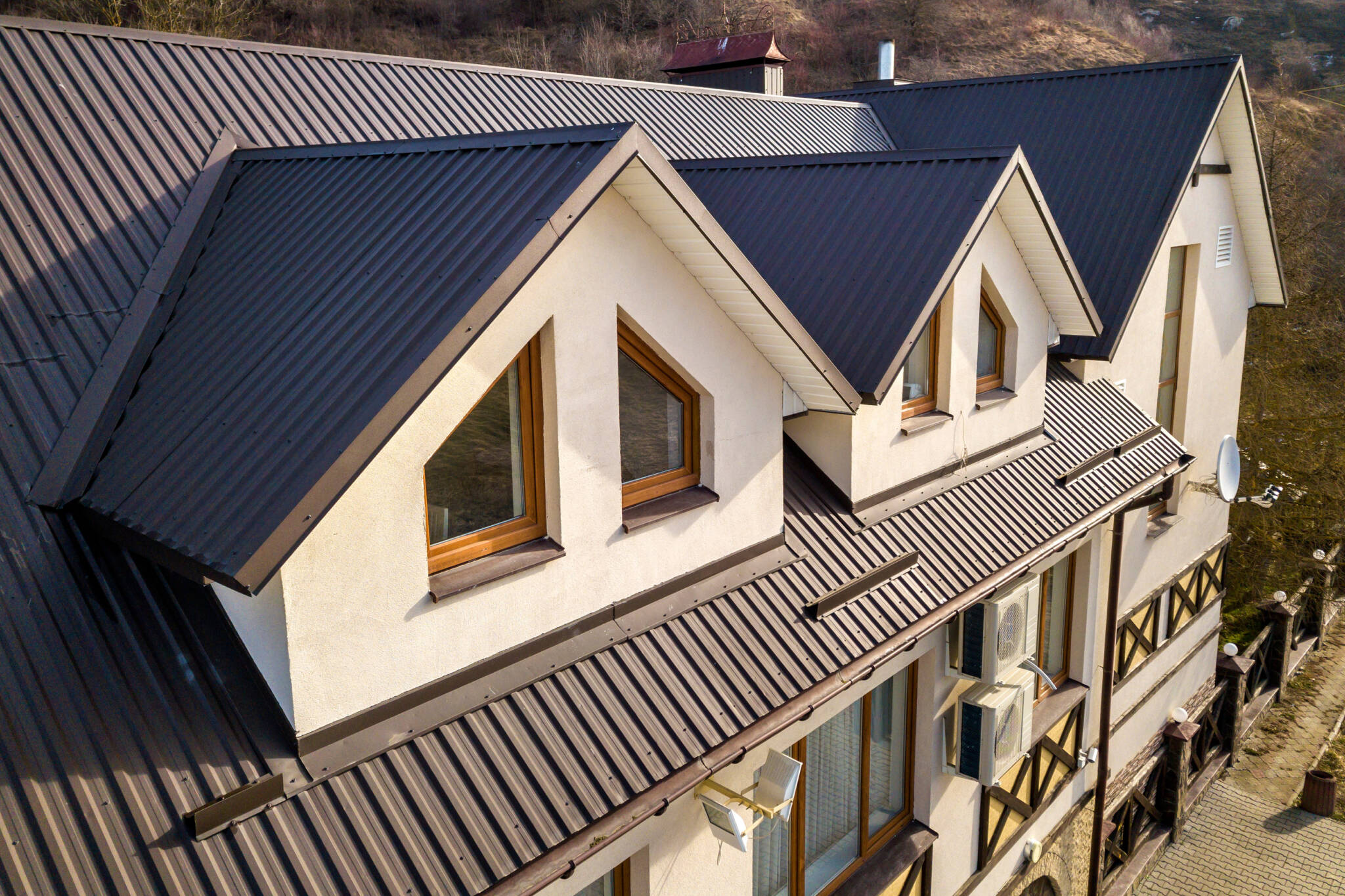 Close Up Aerial View Of Building Attic Rooms Exterior On Metal Shingle Roof, Stucco Walls And Plastic Windows.