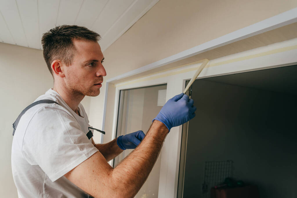 A man pulling painters tape off of a window where caulk has been placed