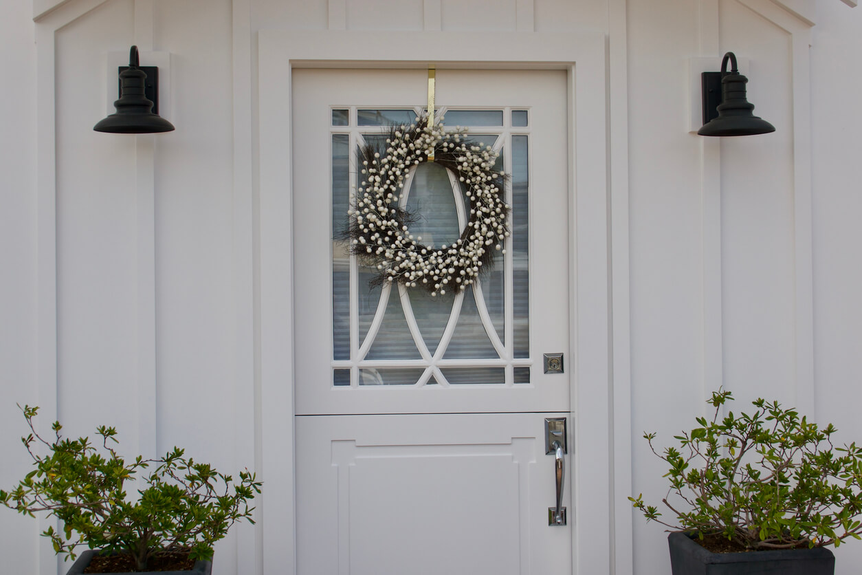 a white and green wreath is hung over a white door using a shiny, gold wreath