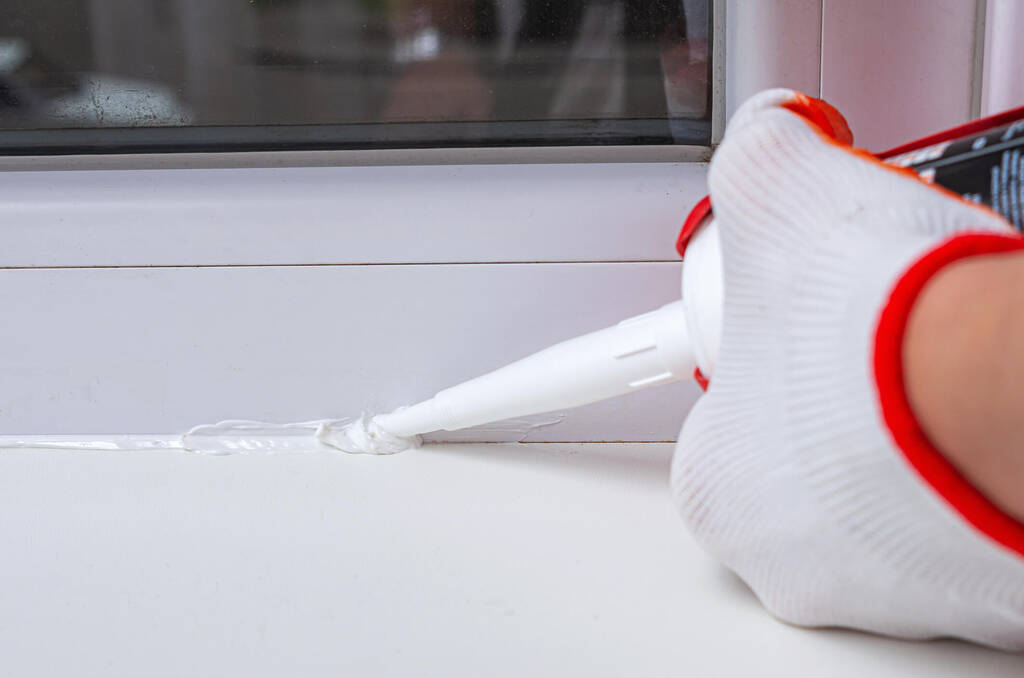close up of hands applying white caulk bead along windowsill