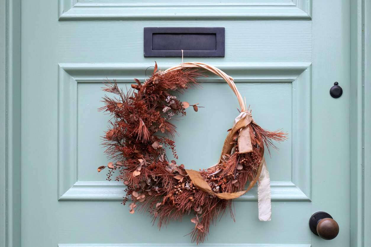 small fall-themed wreath hung from string using the mail slot of a light teal door.